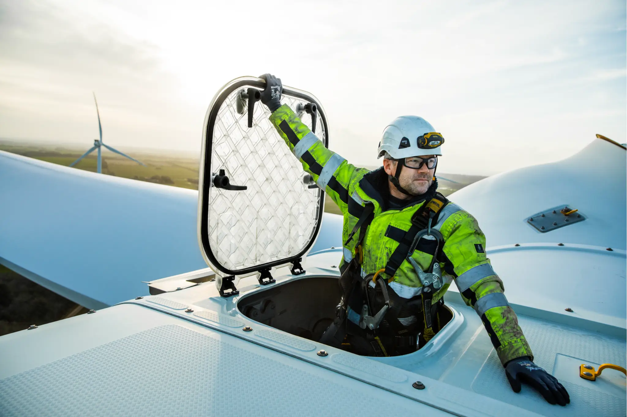 Wind Technician appearing from nacelle hatch at the top of a wind turbine